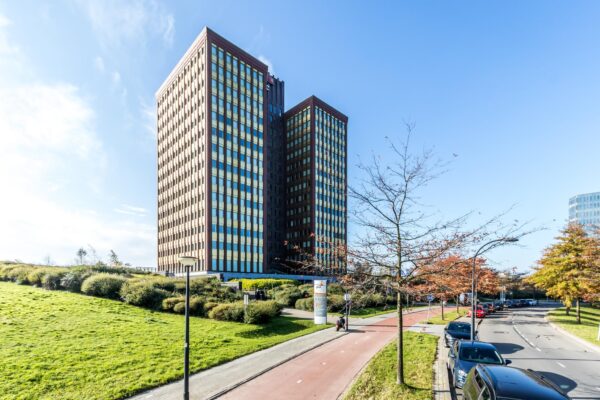 Twee moderne kantoortorens aan de Fascinatio Boulevard met een fietspad, bomen en geparkeerde auto's op de voorgrond.